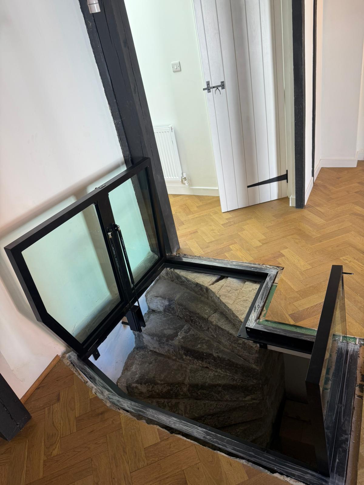 Hinged glass floor doors open revealing stone staircase descent, herringbone parquet flooring, period property Burwash East Sussex